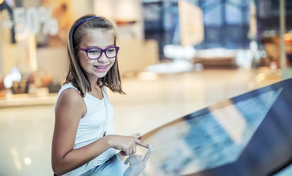 Beautiful cute little girl studying orientation plan in shopping mall. Shopping Center Store Guide. Modern touch screen technology. Toned image