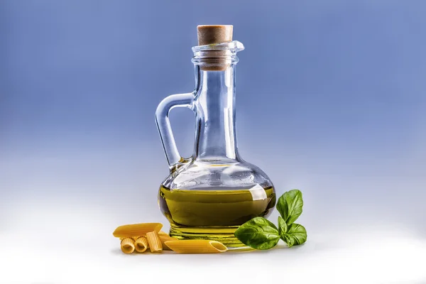 Glass bottle carafe with olive oil penne pasta and basil leaves.