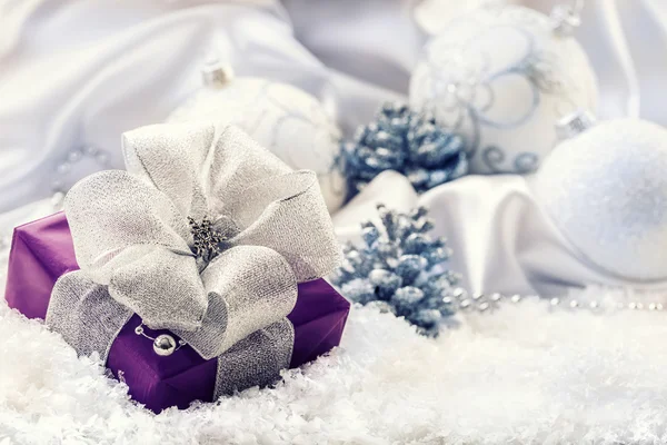 Purple Christmas package with a silver ribbon and background christmas decoration - Christmas balls pine cone white satin and white snow - snowflakes.
