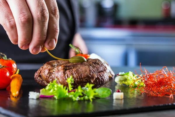 Chef in hotel or restaurant kitchen cooking, only hands. Prepared beef steak with vegetable decoration