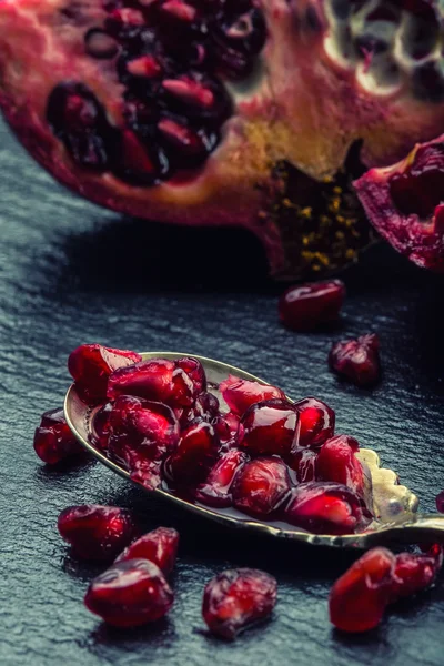 Pieces and grains of ripe pomegranate. Pomegranate seeds. Part of pomegranate fruit on granite board and antique spoon.