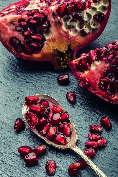 Pieces and grains of ripe pomegranate. Pomegranate seeds. Part of pomegranate fruit on granite board and antique spoon.