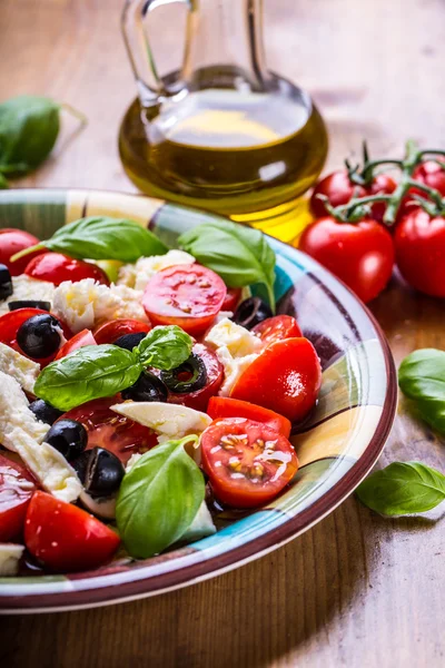 Caprese. Caprese salad. Italian salad. Mediterranean salad. Italian cuisine. Mediterranean cuisine. Tomato mozzarella basil leaves black olives and olive oil on wooden table.