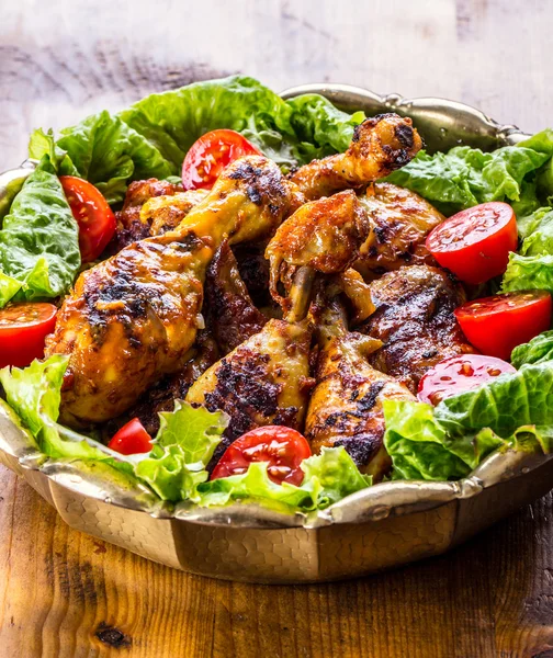 Grilling. Grilled chicken. Grilled chicken legs. Grilled chicken legs, lettuce and cherry tomatoes. Traditional cuisine.