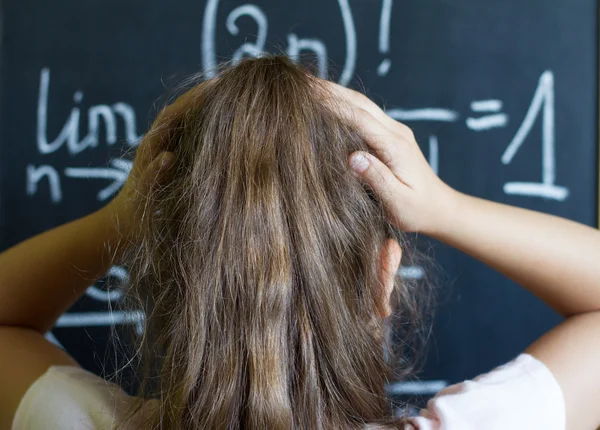 Schoolgirl thinks on the difficult task of mathematics on blackboard