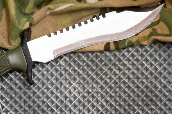 Combat knife on military camouflage fabric and metal background concept