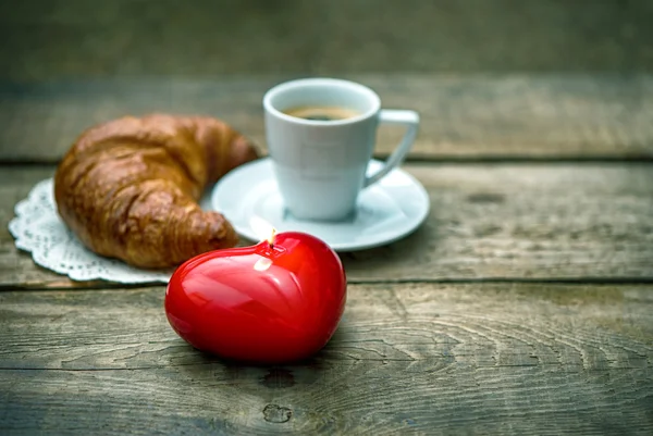 Red heart candle, cup of black coffee with croissant