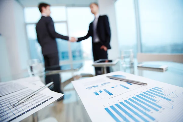 Business document with chart with businessmen handshaking