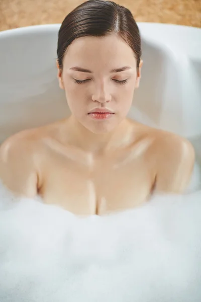 Woman lying in hot bath with foam