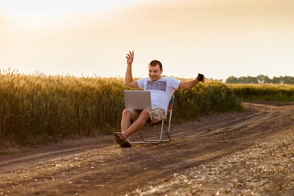 Businessman sitting in the field and working on laptop.