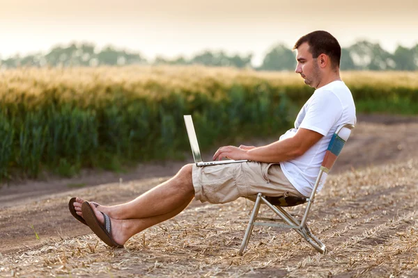 Businessman sitting in the field and working on laptop.