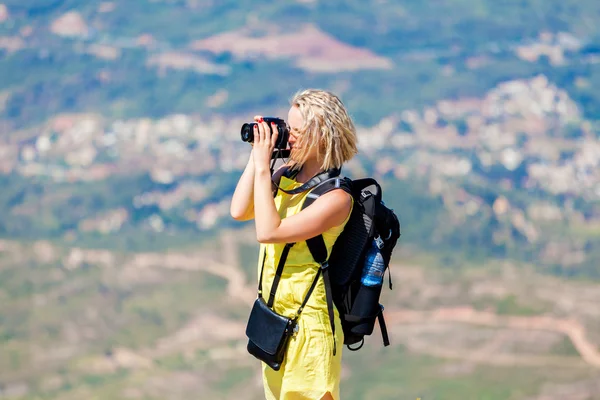 Female traveler stands on hill and takes pictures