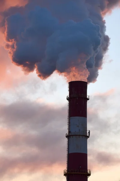 Factory chimney with smokes at sunset