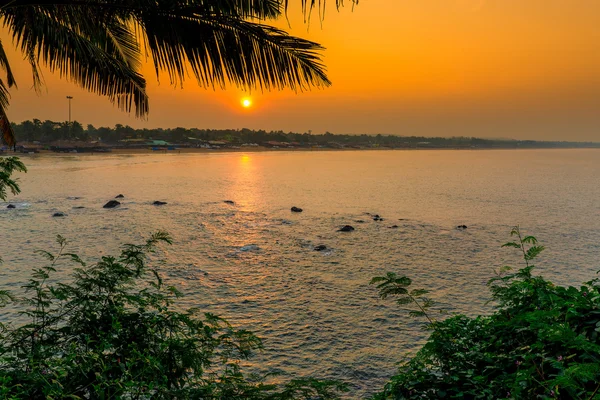 Orange sun at sunrise over the sea and palm leaf
