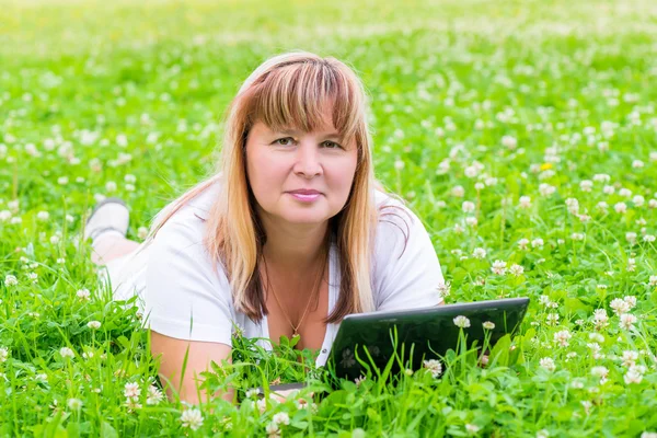 Female 50 years lies with a tablet in a flower meadow