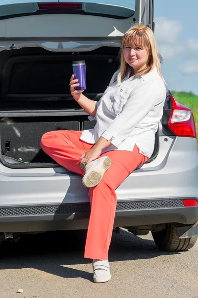 Woman 50 years old with a drink in the car to have a picnic