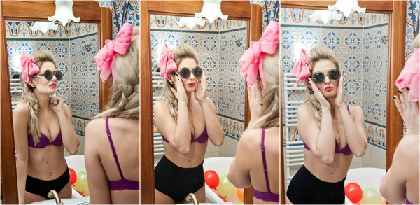 Sexy beautiful young woman wearing black panties and mauve bra looking in the mirror in bathroom. Sensual blonde with sunglasses and big pink ribbon in front of the mirror in elegant bathroom