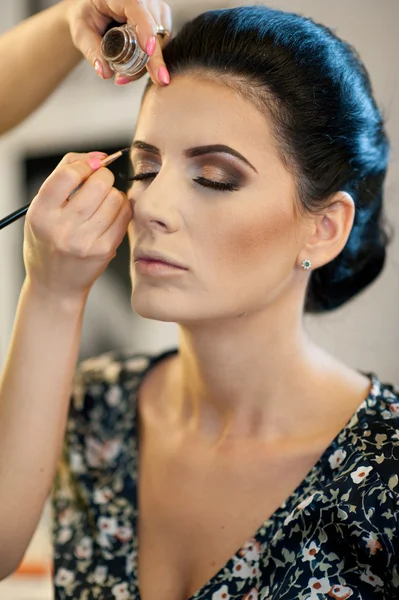 Makeup session with beautiful young brunette woman. Makeup artist doing the eyebrows of an attractive dark hair lady. Makeup artist hand applying dry cosmetic tonal foundation on a face using brush.