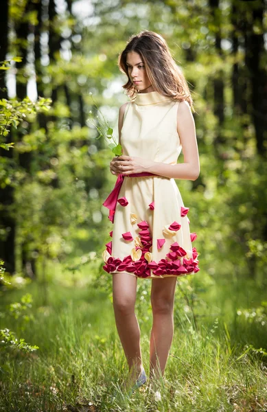 Young beautiful girl in a yellow dress in the woods. Portrait of romantic woman in fairy forest. Stunning fashionable teenage model in summer meadow, outdoor shot. Cute brunette long hair female.
