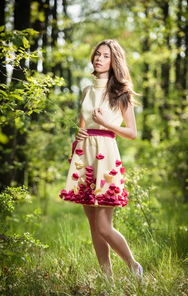 Young beautiful girl in a yellow dress in the woods. Portrait of romantic woman in fairy forest. Stunning fashionable teenage model in summer meadow, outdoor shot. Cute brunette long hair female.