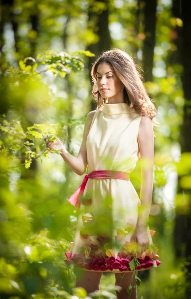 Young beautiful girl in a yellow dress in the woods. Portrait of romantic woman in fairy forest. Stunning fashionable teenage model in summer meadow, outdoor shot. Cute brunette long hair female.