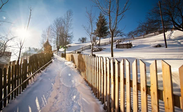 Narrow road covered by snow at countryside. Winter landscape with snowed trees, road and wooden fence. Cold winter day at countryside. Traditional Carpathian mountains village scenery, Romania