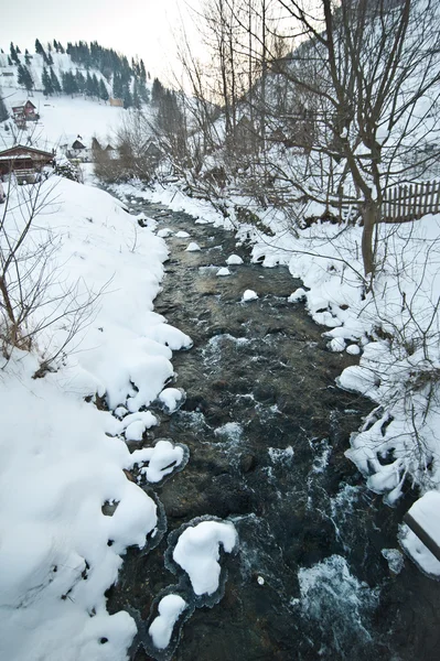 View of frozen river countryside. Brook in snowy landscape. Romanian small river in winter scenery, Romania, Moeciu. Wild brook in winter season.