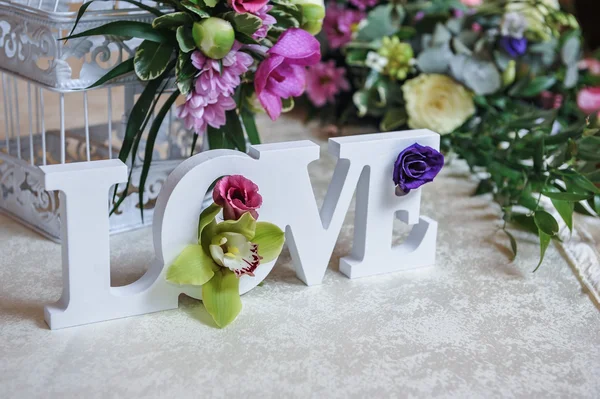 Wedding decor, LOVE letters and flowers on table. Fresh flowers and LOVE decoration on festive table. Luxurious wedding decoration on restaurant table. Elegant event