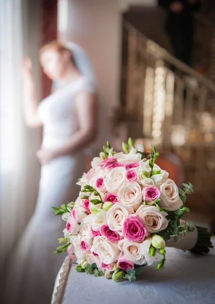 Bride in window frame and wedding bouquet in the foreground. Wedding bouquet with a woman in wedding dress in the background. Beautiful bouquet of white and pink rose flowers. Elegant wedding bouquet