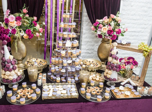 Wedding decoration with multicolored roses in vase, pastel colored cupcakes, meringues, muffins and macarons. Elegant and luxurious event arrangement. Wedding dessert with macaroons and flowers