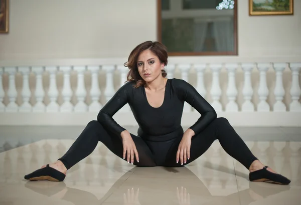 Graceful ballerina doing the splits on the marble floor. Gorgeous ballet dancer performing a split on glossy floor. Short hair young brunette in tight fit ballet outfit making her exercises.