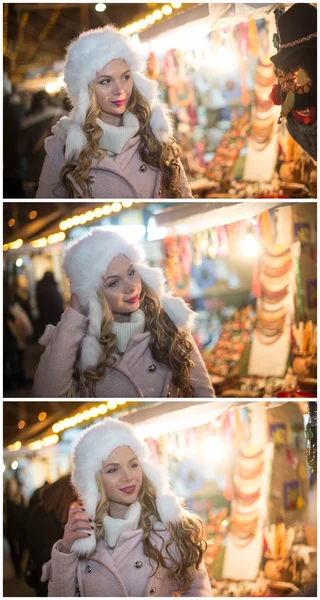 Young woman with white fur cap admiring accessories in Xmas market, cold winter evening. Beautiful blonde girl in winter clothes with Xmas lights in background. Cute female smiling, winter scenery