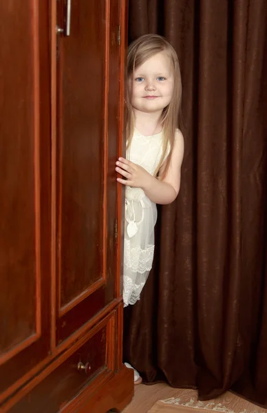 The girl peeks out from behind the wardrobe
