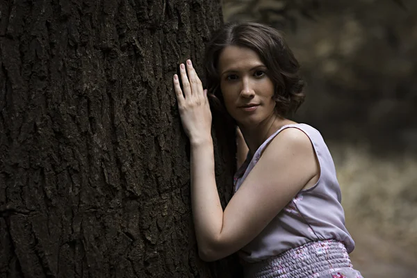 Young woman standing side and resting on tree