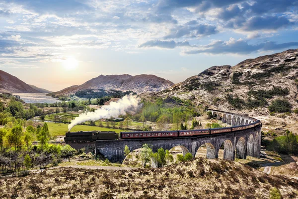 Glenfinnan Railway Viaduct in Scotland with the Jacobite steam train against sunset over lake