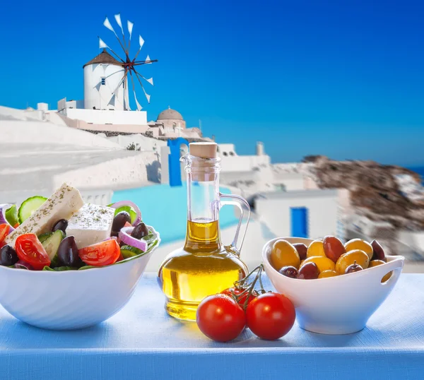 Greek salad against windmill in Oia village, Santorini island in Greece