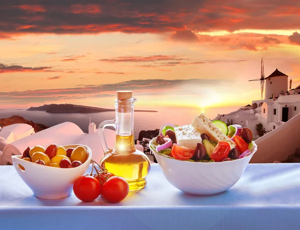 Greek salad against windmill in Oia village, Santorini island in Greece