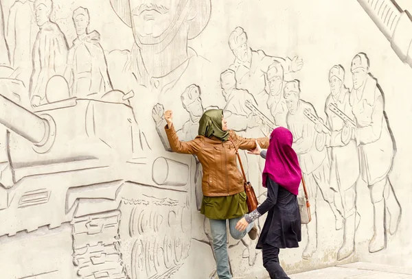 Tourists from Asia pose in front of figures describing feats of