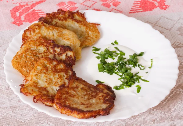 Potato pancakes on a white plate with sour cream and garlic sauc
