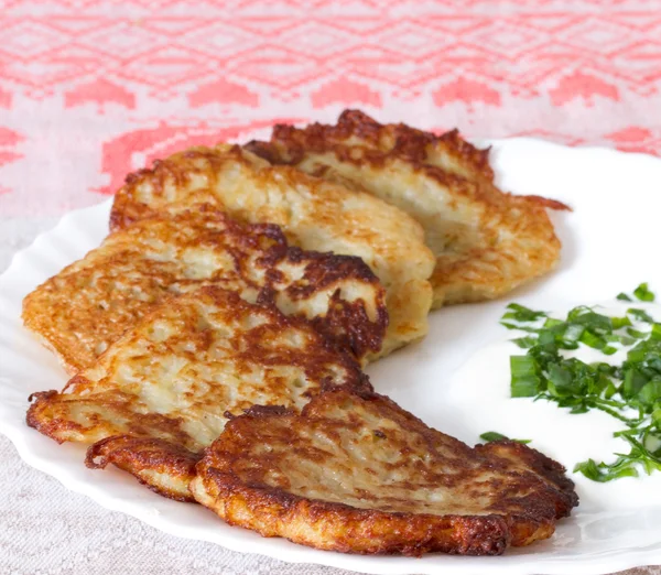 Potato pancakes on a white plate with sour cream and garlic sauc