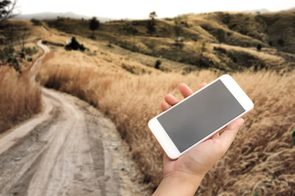 Hand using smartphone on dirt country road.