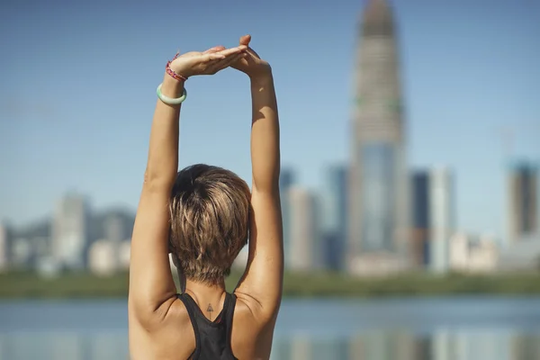 Young woman stretching arms after jogging with skyline background