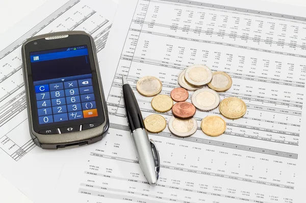 Coins, pen, smartphone in calculator mode on the data table