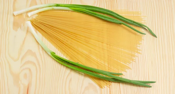 Uncooked long pasta and several green onions on wooden surface