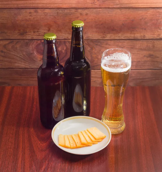 Glass and two bottles of beer, cheese on wooden surface