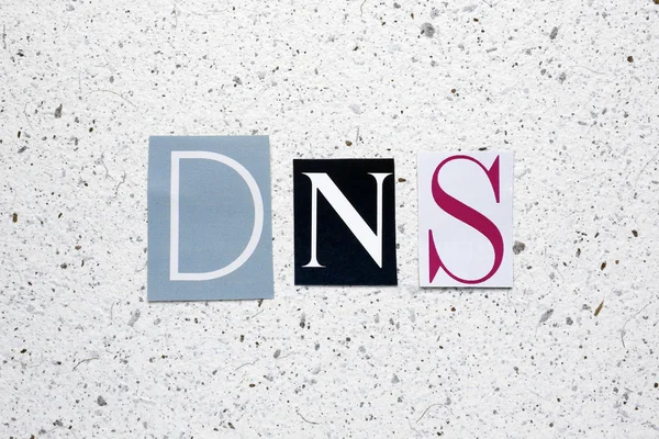 DNS (Domain Name System) acronym cut from newspaper on white handmade paper texture