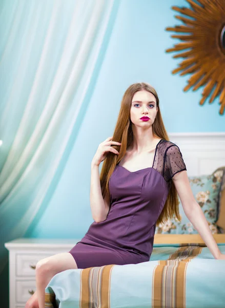 Beautiful woman in purple dress in luxury bedroom interior.