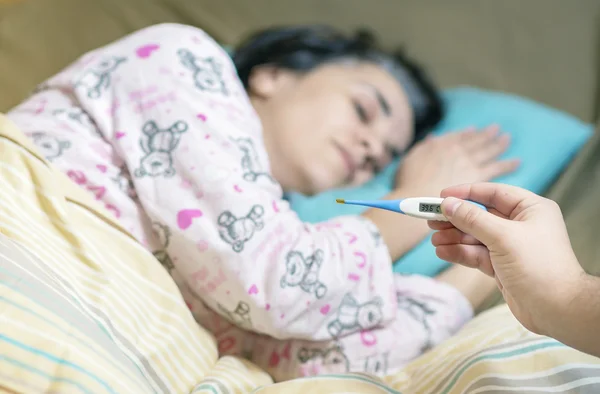 Holding thermometer over a sick woman