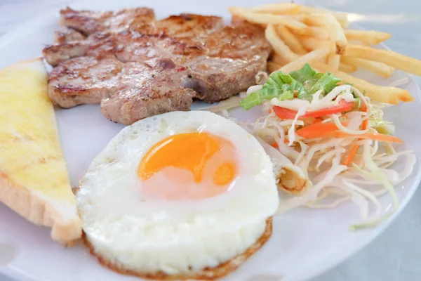 Grilled steaks, French fries, fried egg and vegetables