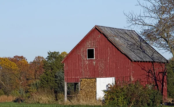 Old country barn outbuilding in fall season with colorful foliage in background.